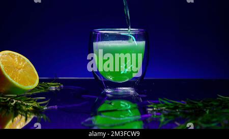 Primo piano di una bevanda da cocktail verde in un bicchiere trasparente posto sul bancone del bar. Clip di scorta. Banco bar decorato con foglie verdi e oran Foto Stock