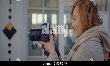Primo piano del fotografo che tiene una fotocamera professionale. Azione. La fotocamera è nelle mani di un giovane fotografo professionista. Donna scatta foto con la fotocamera. Foto Stock