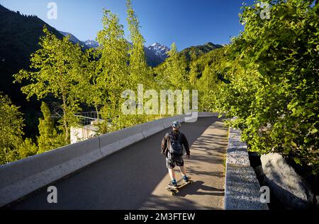 Uomo Skater nel casco cavalcare sulla strada di montagna al suo longboard vicino boschetto di legno di betulla e la cima della neve al Kazakhstan mattina d'estate Foto Stock