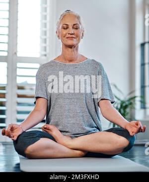 La meditazione è ottima per molte cose. una donna matura allegra che pratica yoga mentre medita all'interno di uno studio durante il giorno. Foto Stock