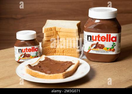 Nutella con bottiglie grandi e piccole e un po' di pane bianco ordinato sul tavolo da pranzo Foto Stock