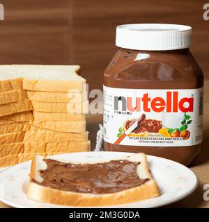 Nutella con bottiglie grandi e piccole e un po' di pane bianco ordinato sul tavolo da pranzo Foto Stock