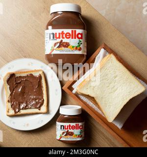 Nutella con bottiglie grandi e piccole e un po' di pane bianco ordinato sul tavolo da pranzo Foto Stock