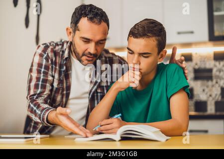 Padre sta aiutando suo figlio con l'apprendimento. Stanno facendo i compiti insieme. Foto Stock