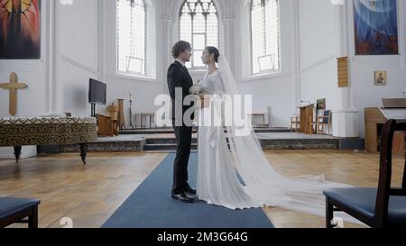 Il Tempio Bianco. Action.A bella giovane coppia in costumi da matrimonio e un bouquet di fiori che sono sposati in una chiesa con grandi croci e icona Foto Stock
