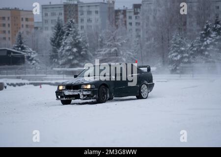 12-12-2022 riga, Lettonia un'auto parcheggiata nella neve di fronte ad un edificio con una luce rossa sul suo faro. . Foto Stock