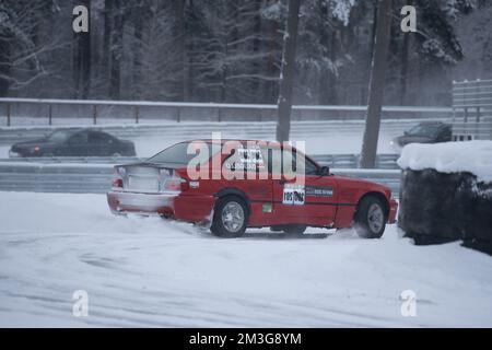 12-12-2022 riga, Lettonia una macchina rossa sta guidando attraverso la neve in un parcheggio con un cartello sul suo parabrezza. . Foto Stock