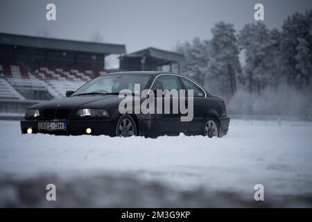 12-12-2022 riga, Lettonia un'auto nera parcheggiata nella neve vicino ad uno stadio nella neve con un bleacher rosso e bianco. . Foto Stock