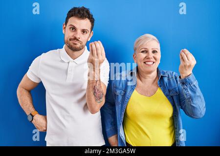Giovane madre brasiliana e figlio in piedi su sfondo blu facendo gesto italiano con mano e dita espressione fiduciosa Foto Stock