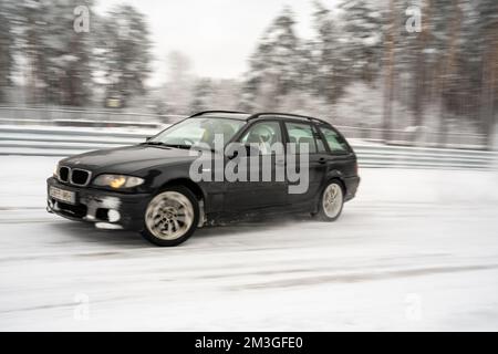 12-12-2022 riga, Lettonia un'auto nera che guida lungo una strada innevata vicino agli alberi e una recinzione con neve sui suoi lati. . Foto Stock