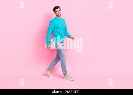 Foto a grandezza naturale di un giovane ragazzo attraente che tiene un laptop che cammina sorriso toothy indossare abiti blu alla moda isolato su sfondo di colore rosa Foto Stock
