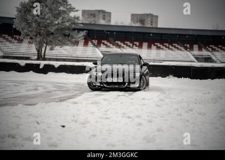 12-12-2022 riga, Lettonia una macchina nera parcheggiata nella neve vicino a uno stadio bleachers e alberi con neve a terra. . Foto Stock