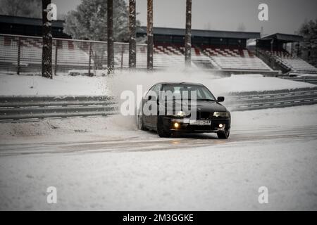 12-12-2022 riga, Lettonia un'auto che guida lungo una strada innevata di fronte ad uno stadio con neve a terra e una recinzione. . Foto Stock