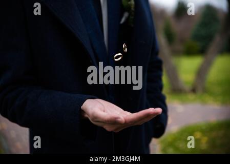 Sposo che tiene gli anelli di nozze in mano. Due anelli per matrimoni sul pavimento con anelli per matrimoni a contrasto sul pavimento, sul piano terra, al pianoforte, a portata di mano. groom che lancia Foto Stock