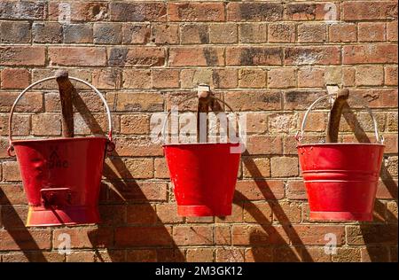 Tre secchi rossi appesi su grandi ganci su un muro di mattoni Foto Stock