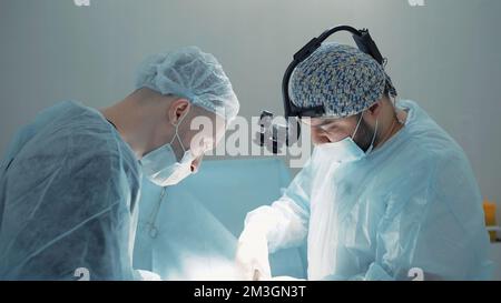 Due chirurghi occupati al lavoro . Azione . Due uomini in camici da laboratorio blu stanno lavorando con cura ad un'operazione complessa , utilizzando vari accessori medici li Foto Stock