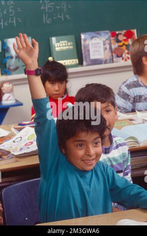 Ragazzo ispanico in classe alzando la mano per essere chiamato dall'insegnante Foto Stock