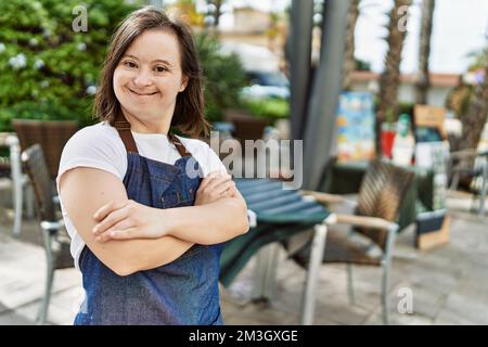 Giovane giù sindrome donna sorridente sicuro indossare grembiule al bar terrazza Foto Stock