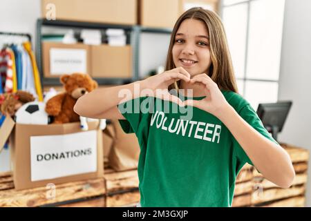 Adorabile ragazza che indossa uniforme volontaria facendo il simbolo del cuore con le mani al centro di carità Foto Stock