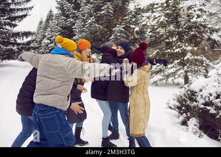 Amici allegri abbracciano e ridono mentre si divertono nel parco cittadino coperto di neve o nella foresta invernale. Foto Stock