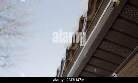 Tetto invernale. Action.A paesaggio dove si possono vedere grandi ciclicoli che gocciolano appeso in cima alla casa e si può vedere il cielo blu. Alta qualità 4 Foto Stock