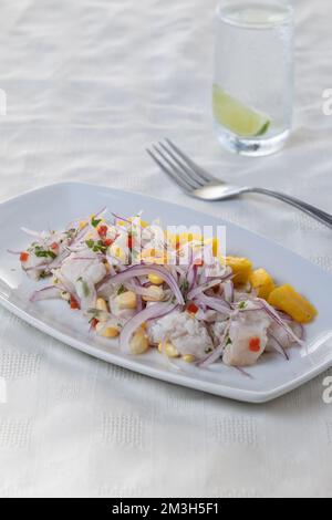 Ceviche, piatto tipico a base di pesce della cucina peruviana, presentato in un piatto rettangolare su un tavolo con tovaglia bianca. Foto Stock