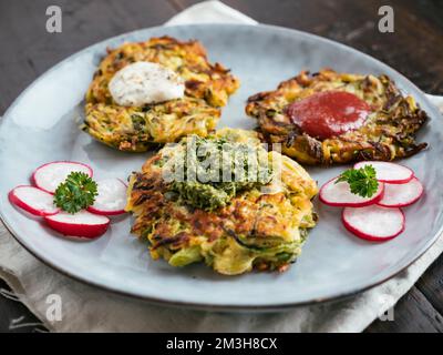 Frittelle di zucchine vegane fatte in casa con tre salse. Foto Stock