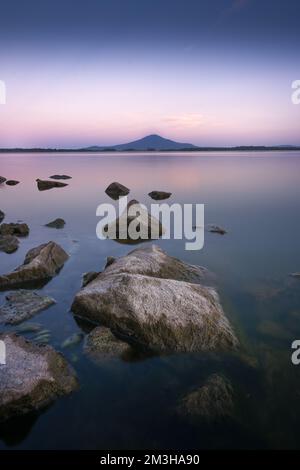 Un bellissimo paesaggio di un lago con pietre in primo piano, una montagna sullo sfondo e un bel cielo viola Foto Stock