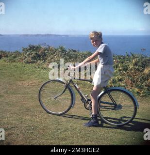 1960s, storico, un ragazzo adolescente sulla sua bicicletta dell'epoca, una Jeep Hercules, su un sentiero erboso che domina la costa, Inghilterra, Regno Unito, il giovane, che indossa un top a maniche corte, pantaloncini e plimsoll blu, è seduto a cavallo della mini-roadster inglese, che ha una pompa per bicicletta sul telaio. Foto Stock