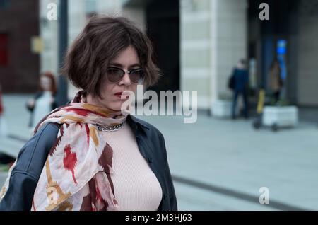 Una donna triste in occhiali da sole scuri cammina lungo la strada della città Foto Stock