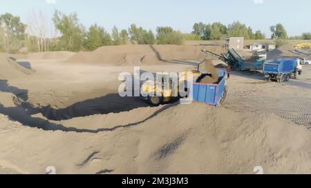 Serbia, Belgrado - 30 luglio 2021: L'escavatore riempie la terra nel camion di scarico. Scenografia. Cantiere con autocarri e escavatori o attività minerarie. Looting Foto Stock