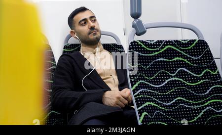 Ritratto di un bell'uomo in cuffia che ascolta musica con i mezzi pubblici. Media. Giovane uomo in autobus vuoto guardando pensieroso Foto Stock