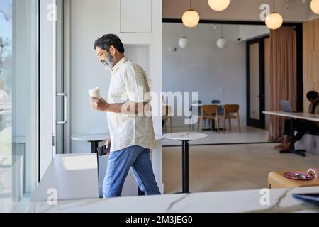 Uomo maturo sorridente con una tazza da caffè usa e getta che lascia la caffetteria Foto Stock