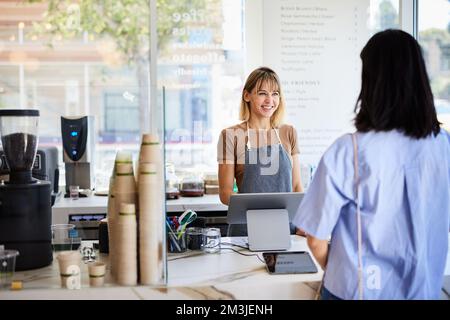 Sorridente proprietario che parla con una cliente femmina al banco cassa Foto Stock