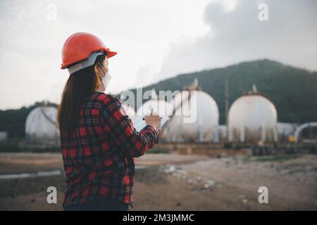 Donna operatrice asiatica felice nell'industria chimica del petrolio che lavora elenco di ispezione visiva sulla clipboard in pianta Foto Stock