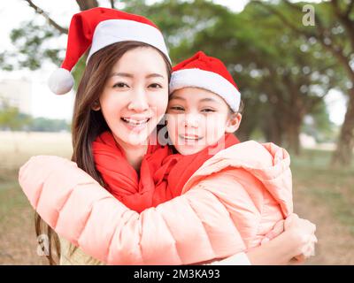 Felice madre e figlia abbracciando e indossando cappelli rossi di babbo natale Foto Stock