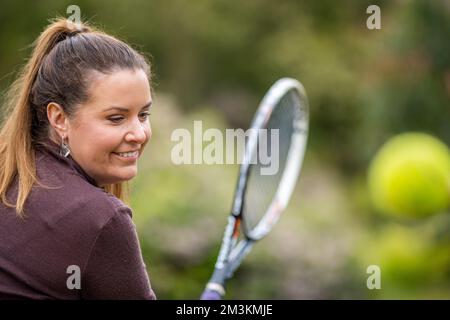 tennista femminile che pratica le mani in avanti e che colpisce le palle da tennis su un campo d'erba in inghilterra Foto Stock