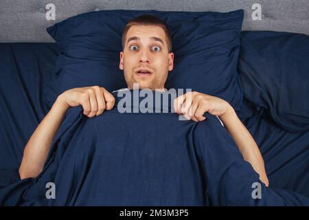 Guardando direttamente nel telaio. Un bel giovane ragazzo che si nasconde dietro una coperta guarda al lato. Direzione dello sguardo in direzioni diverse. Foto Stock