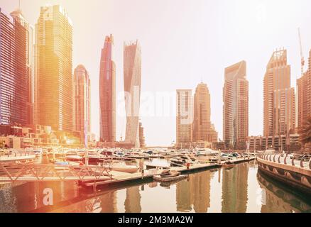 Vista degli alti edifici del quartiere residenziale di Dubai Marina e yacht ormeggiati vicino al molo in giorno di sole. Dubai Marina Towers. Flare sole, film Foto Stock