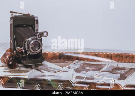 Un'antica macchina fotografica si erge su un tavolo di legno tra film fotografici e fotografie. Foto Stock