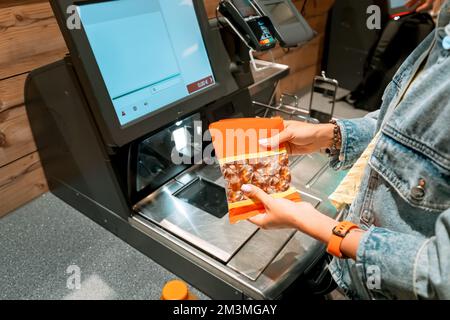 Una ragazza cliente scanns e paga le merci da un supermercato in un terminale automatizzato di controllo self-service Foto Stock