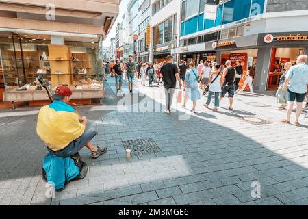 30 luglio 2022, Colonia, Germania: Un rifugiato dalla guerra in Ucraina, un musicista suona sulla strada della città, avvolto nella bandiera Ucraina Foto Stock