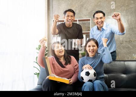 Gli amici guardano gli sport in TV, festeggiano e festeggiano. Felici tifosi diversi amici asiatici sedersi sul divano con popcorn e bevande Foto Stock