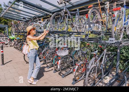 30 luglio 2022, Colonia, Germania: Ragazza ciclista al parcheggio intercetta a due piani per biciclette vicino al centro dei trasporti della città. Deposito sicuro e bicicletta in Foto Stock