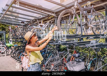 Ragazza ciclista al parcheggio intercept a due piani per biciclette vicino al centro dei trasporti della città. Deposito sicuro e infrastrutture per biciclette in una città moderna Foto Stock