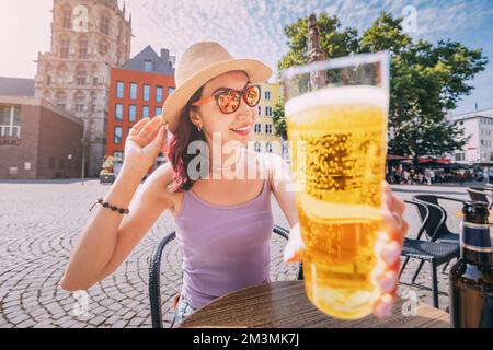 Una ragazza beve e assaggia un delizioso tipo di artigianato tradizionale tedesco e birra di Colonia Kolsch in un pub o caffetteria che si affaccia sulla piazza della città vecchia Foto Stock