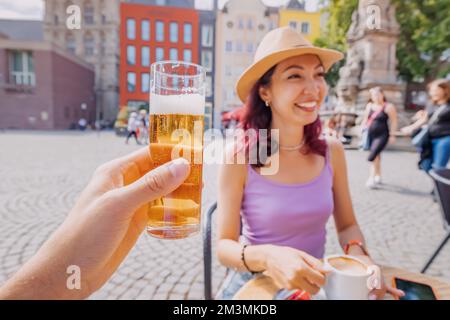 Mano con la birra kolsch e la ragazza che beve il tè in background Foto Stock