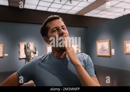 un visitatore o studente annoiato in una galleria d'arte o in un museo si sbadisce e guarda i capolavori delle arti classiche Foto Stock