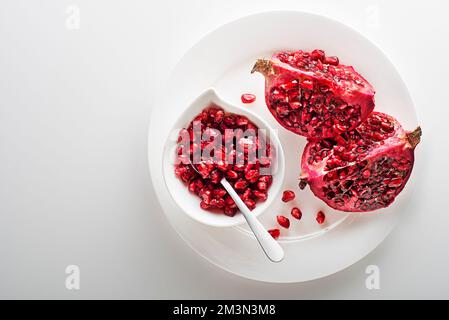 Frutti di melograno sani e maturi, aperti e spelati con semi su piatto bianco Foto Stock