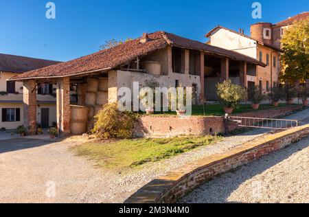 Vecchio fienile con balle rotonde di fieno sotto un ampio portico di travi in legno e tegole tipiche della campagna in provincia di Cuneo, Piemonte, Italia Foto Stock